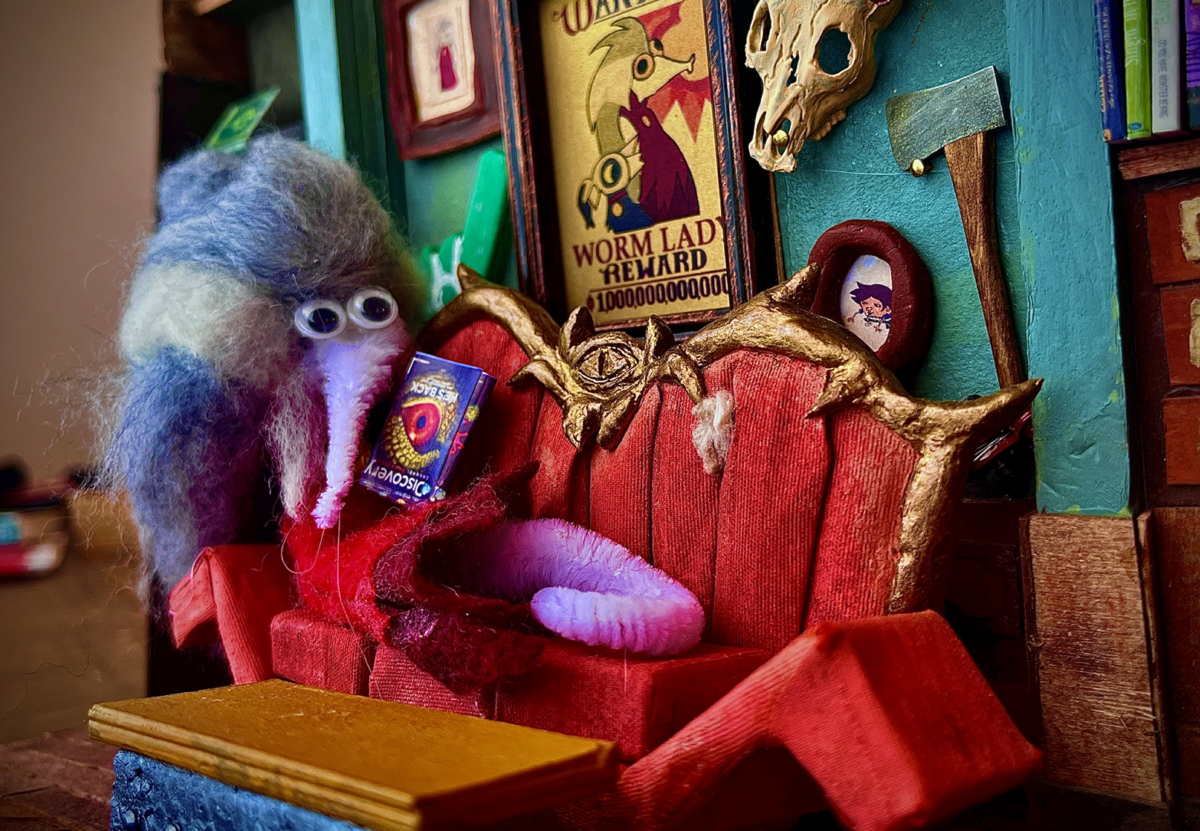 A Fuzzy worm of Eda from the Owl House sitting on a couch and reading.