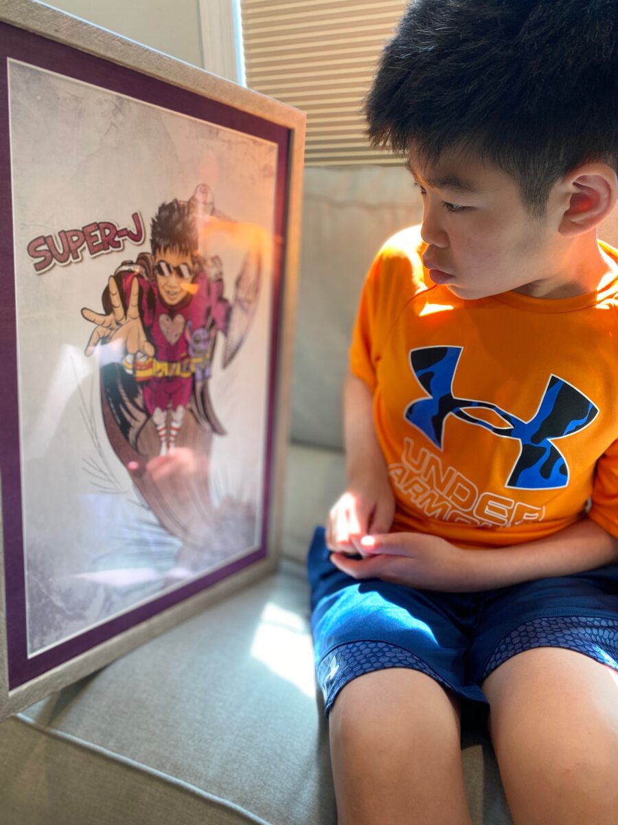 Photo of a child holding a poster of the superhero self they created and was designed by an artist.